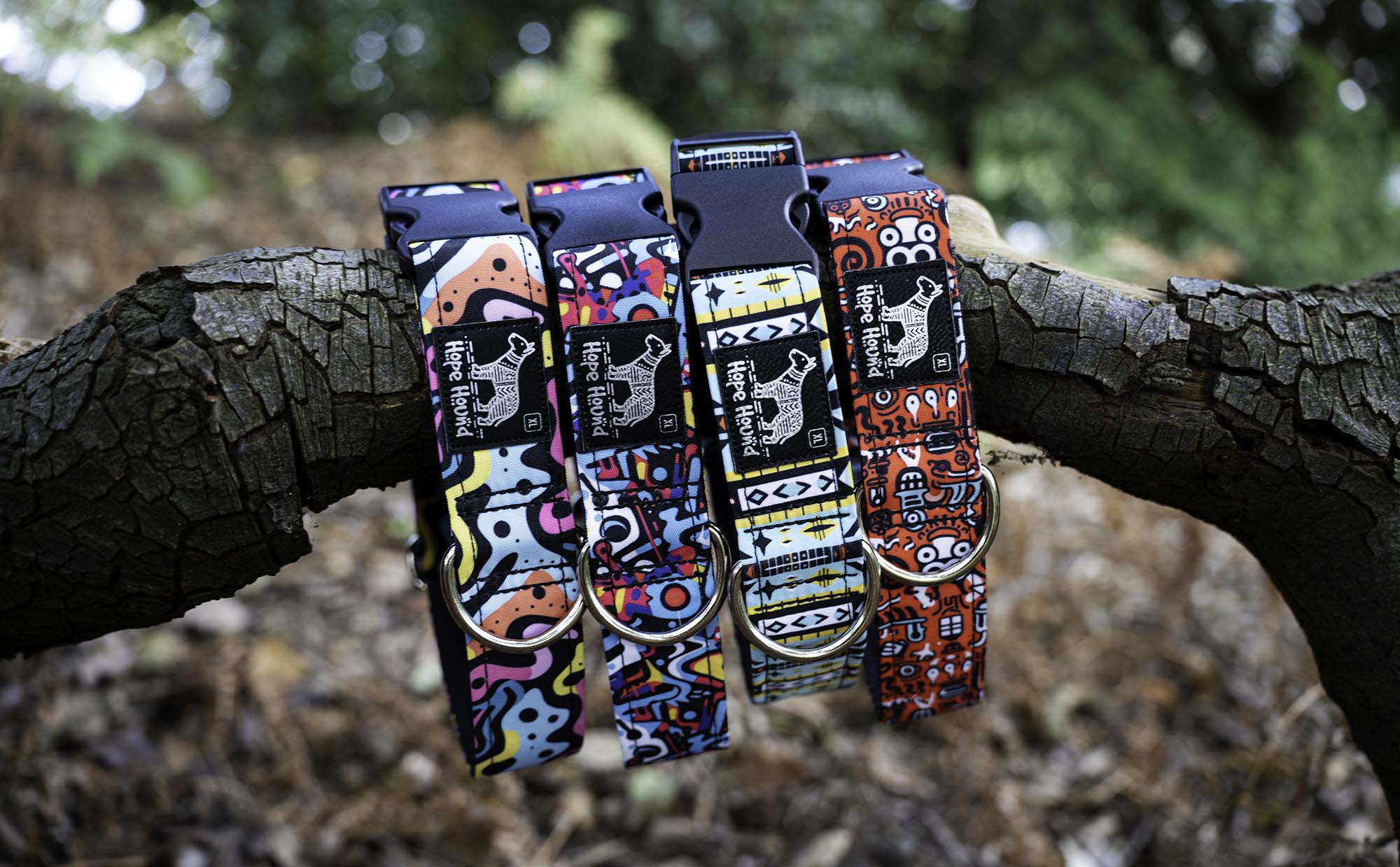 Four colorful dog collars with unique patterns hanging on a tree branch.